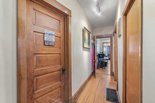 hallway featuring rail lighting, light wood-style flooring, visible vents, and baseboards