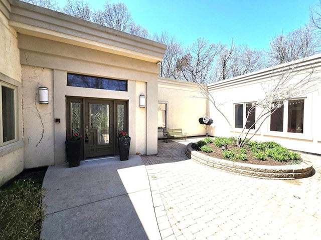 view of exterior entry with stucco siding and a patio area