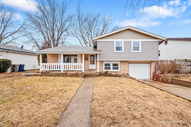 tri-level home with brick siding, a porch, an attached garage, a front yard, and driveway