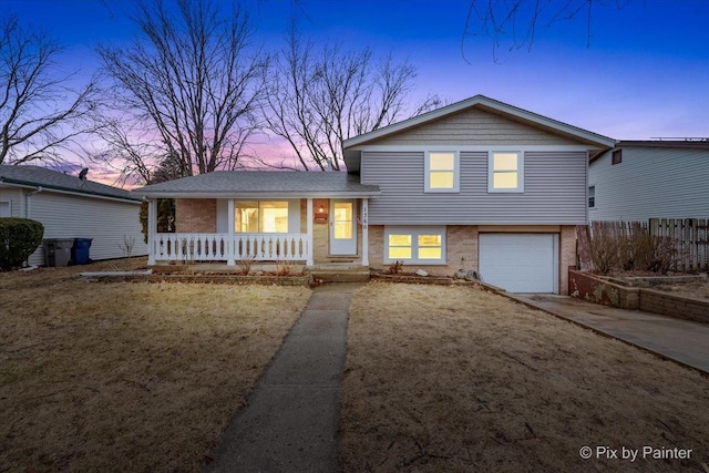 tri-level home featuring driveway, covered porch, an attached garage, and brick siding