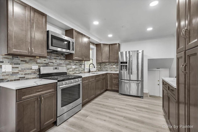 kitchen featuring light wood finished floors, decorative backsplash, appliances with stainless steel finishes, dark brown cabinetry, and light stone countertops