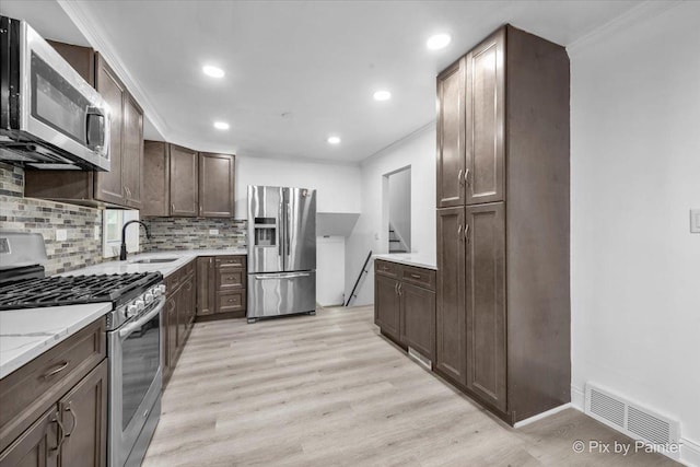 kitchen featuring visible vents, backsplash, appliances with stainless steel finishes, dark brown cabinets, and light wood-type flooring