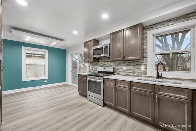 kitchen with decorative backsplash, light wood-style flooring, stainless steel appliances, dark brown cabinets, and a sink