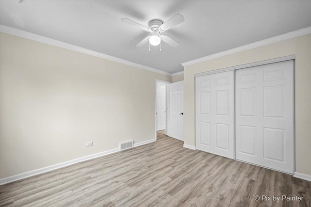 unfurnished bedroom featuring crown molding, a closet, visible vents, wood finished floors, and baseboards