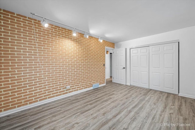 below grade area featuring baseboards, visible vents, brick wall, and wood finished floors