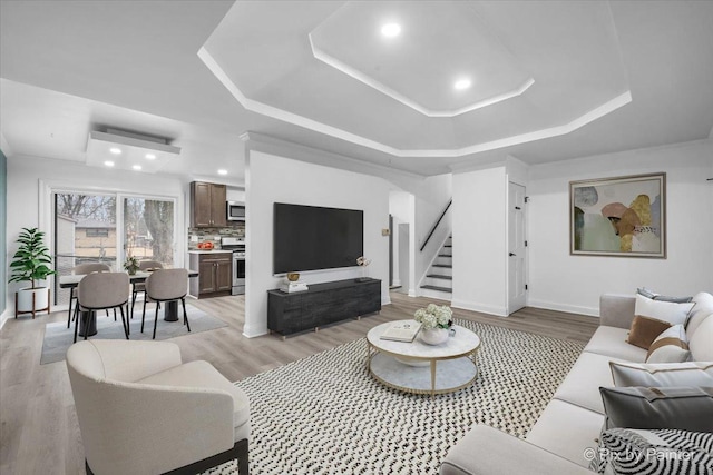 living room featuring light wood-style floors, a tray ceiling, and stairway