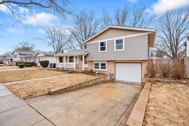 split level home featuring a garage, driveway, brick siding, and a porch