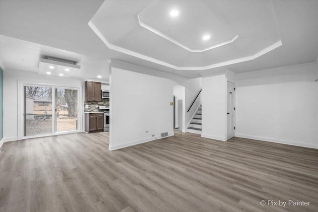 unfurnished living room featuring a tray ceiling, stairway, baseboards, and wood finished floors