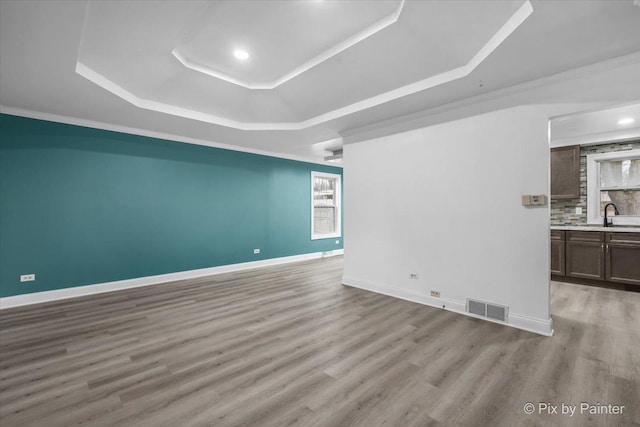 empty room with a raised ceiling, visible vents, baseboards, and light wood finished floors