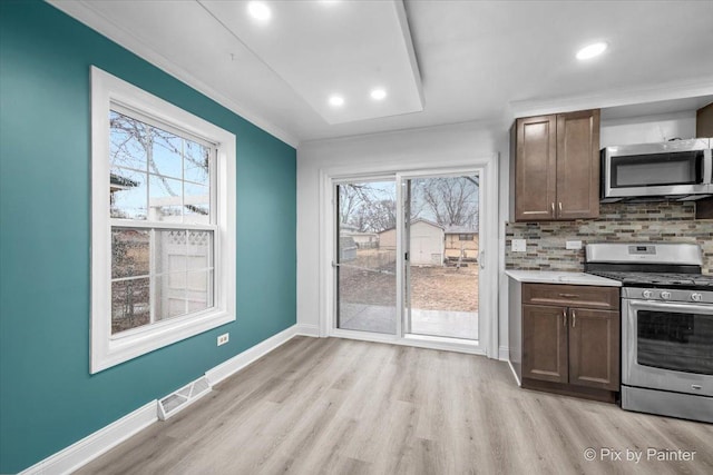 kitchen featuring light wood finished floors, stainless steel appliances, visible vents, decorative backsplash, and baseboards