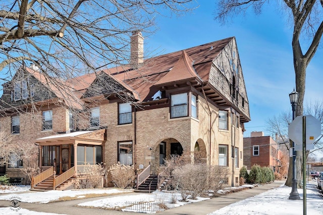 view of front of house featuring a sunroom, a chimney, and brick siding