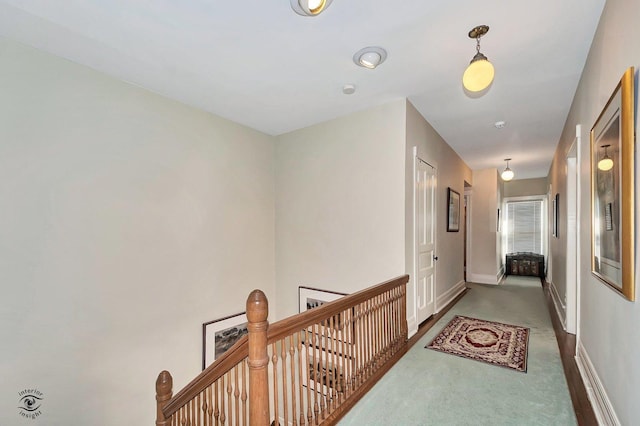 hallway with carpet floors, baseboards, and an upstairs landing