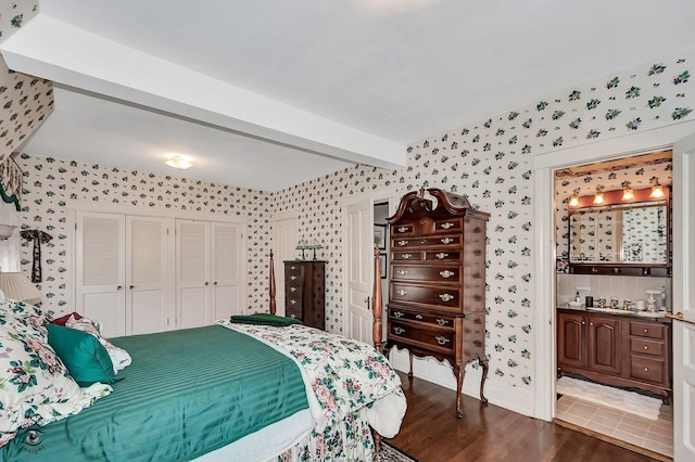 bedroom featuring dark wood-style flooring, a closet, beam ceiling, ensuite bath, and wallpapered walls