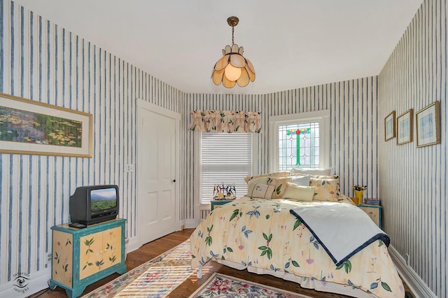 bedroom with baseboards, wood finished floors, and wallpapered walls