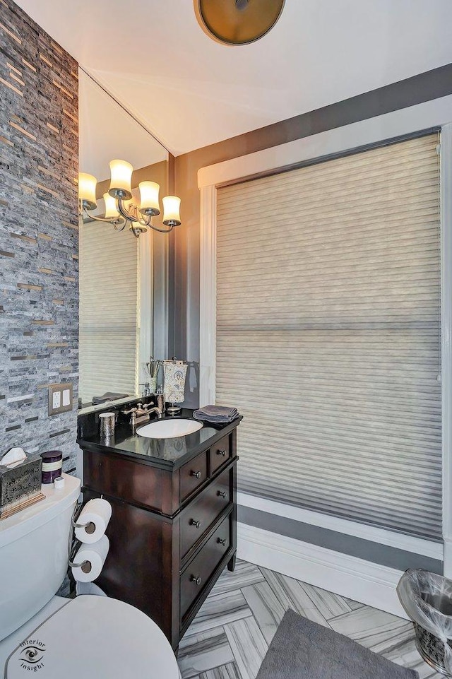 half bathroom with vanity, toilet, and an inviting chandelier