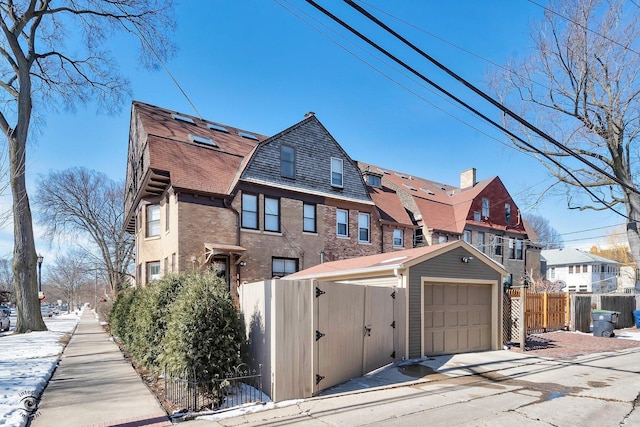 view of front facade with brick siding, a gambrel roof, a gate, fence, and a garage