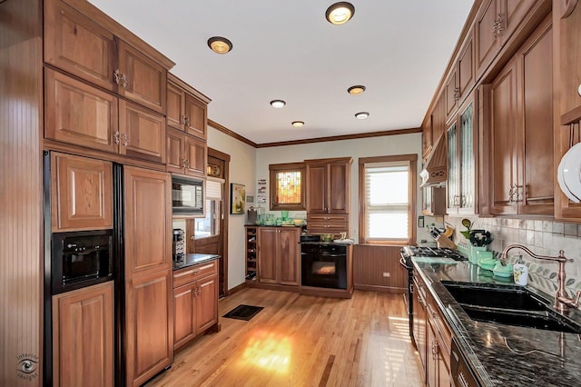 kitchen featuring light wood-style floors, brown cabinets, crown molding, black appliances, and a sink