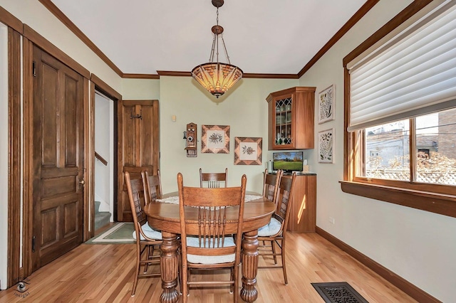 dining area with light wood-style floors, visible vents, ornamental molding, and baseboards