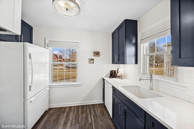 kitchen featuring tasteful backsplash, baseboards, light stone counters, white appliances, and a sink