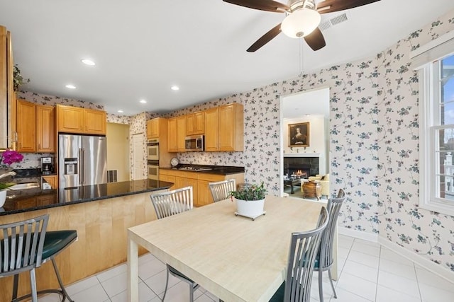 kitchen with light tile patterned floors, stainless steel appliances, a tiled fireplace, plenty of natural light, and wallpapered walls