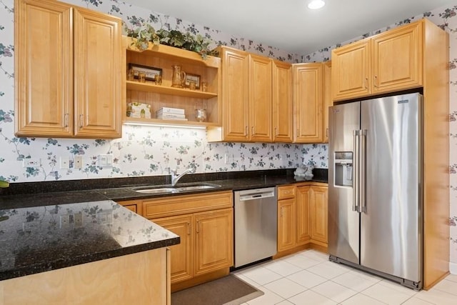 kitchen featuring wallpapered walls, dark stone counters, stainless steel appliances, and a sink