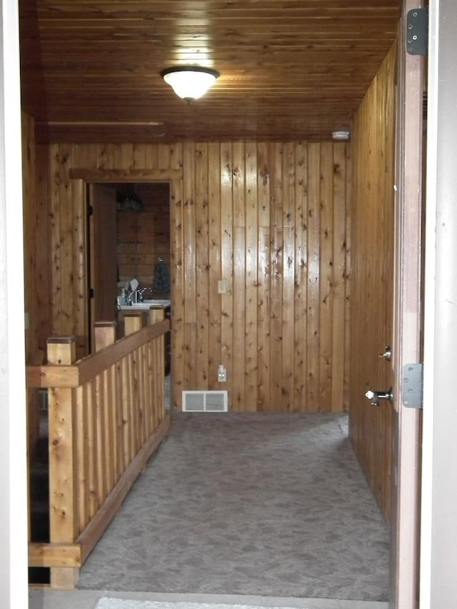 carpeted spare room featuring wooden ceiling, wooden walls, and visible vents