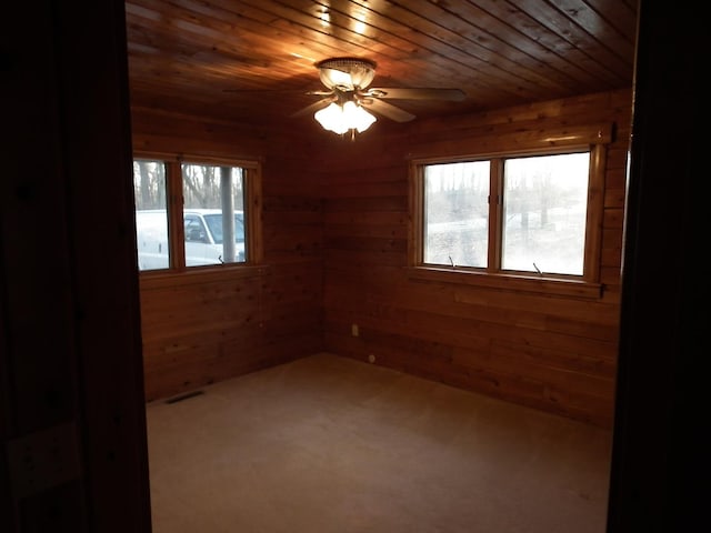 empty room featuring carpet, visible vents, a ceiling fan, wood ceiling, and wooden walls