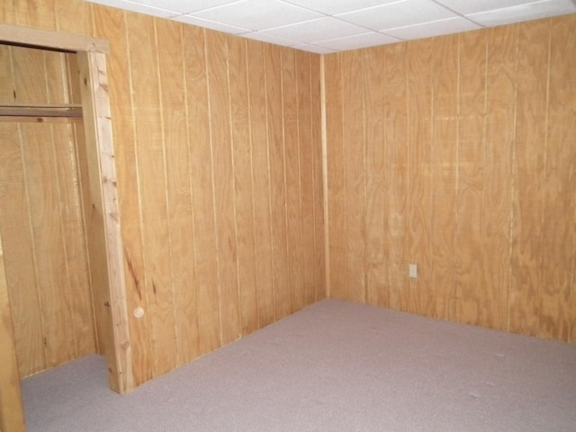 carpeted empty room featuring wood walls and a drop ceiling