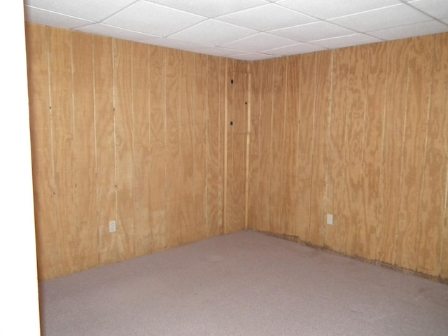 carpeted empty room featuring a paneled ceiling and wood walls