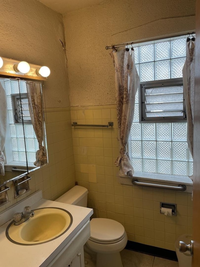 bathroom featuring toilet, a wainscoted wall, tile walls, vanity, and tile patterned floors