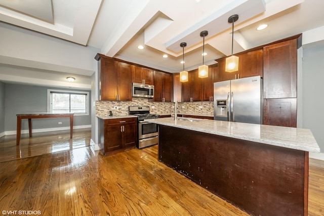 kitchen featuring a center island with sink, backsplash, appliances with stainless steel finishes, dark wood-type flooring, and a sink