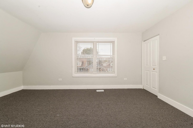 interior space with vaulted ceiling, dark carpet, and baseboards