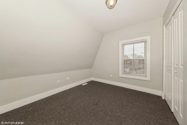 bonus room with dark colored carpet, lofted ceiling, and baseboards