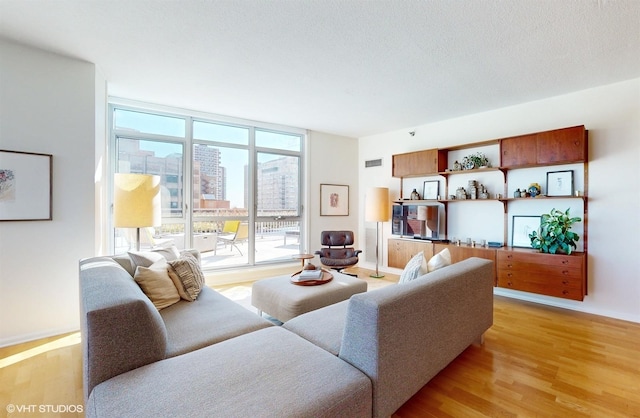 living room with a wall of windows, light wood-style floors, visible vents, and a textured ceiling