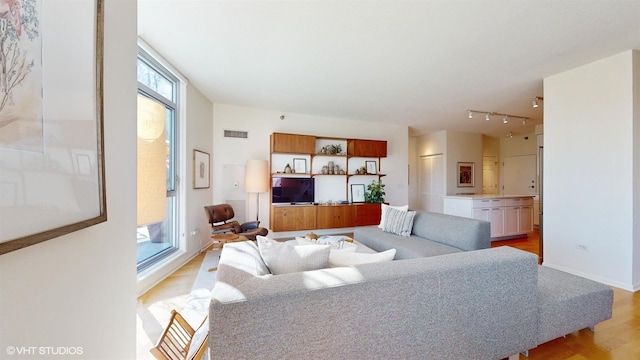 living area featuring track lighting, baseboards, light wood-type flooring, and visible vents