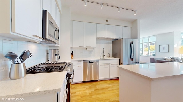 kitchen featuring tasteful backsplash, open floor plan, white cabinetry, light wood-style floors, and appliances with stainless steel finishes