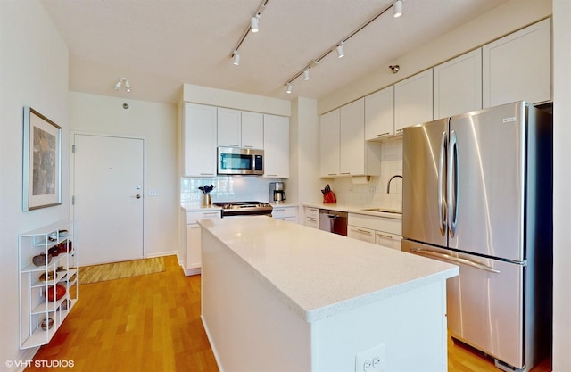 kitchen featuring a center island, decorative backsplash, light wood-style flooring, appliances with stainless steel finishes, and a sink