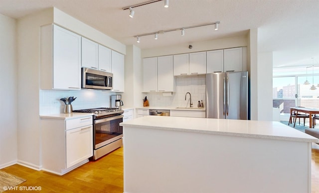 kitchen with light wood finished floors, a center island, decorative backsplash, appliances with stainless steel finishes, and a sink