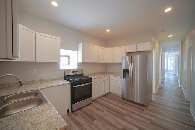 kitchen with white cabinets, wood finished floors, stainless steel appliances, light countertops, and a sink