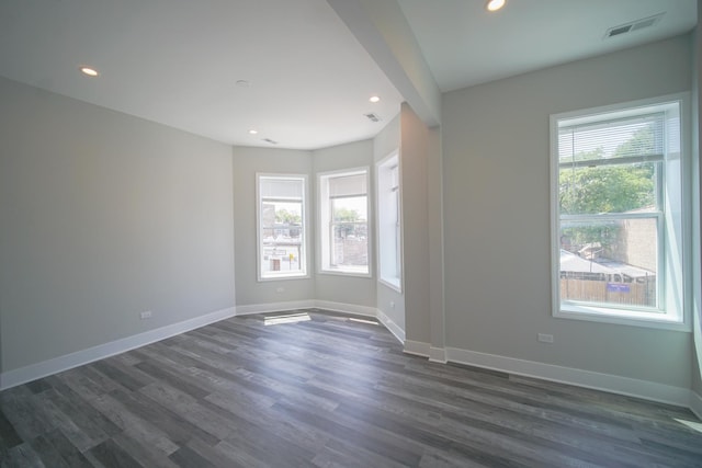 unfurnished room with a wealth of natural light, dark wood-style flooring, visible vents, and baseboards