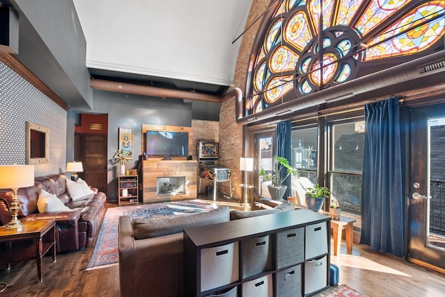 living room featuring a high ceiling, visible vents, a fireplace, and wood finished floors