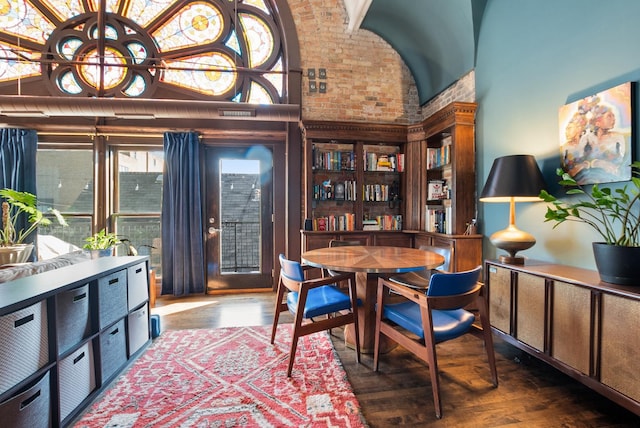 dining space featuring a towering ceiling, brick wall, and wood finished floors