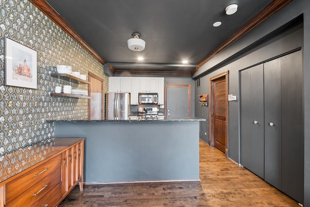 kitchen with crown molding, stainless steel appliances, white cabinetry, dark stone countertops, and wood finished floors