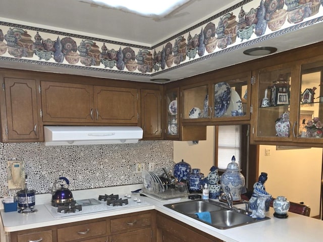 kitchen with white gas stovetop, light countertops, backsplash, a sink, and under cabinet range hood