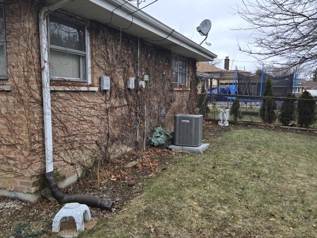 view of side of home with brick siding, fence, central AC, and a yard