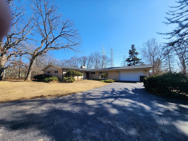 view of front facade with a front lawn, aphalt driveway, an attached garage, brick siding, and a chimney