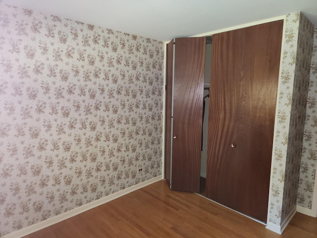 unfurnished bedroom featuring a closet, wallpapered walls, and wood finished floors