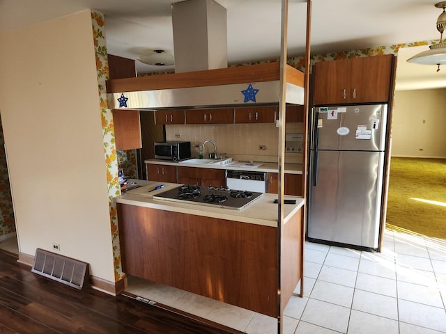 kitchen featuring visible vents, a peninsula, a sink, light countertops, and appliances with stainless steel finishes