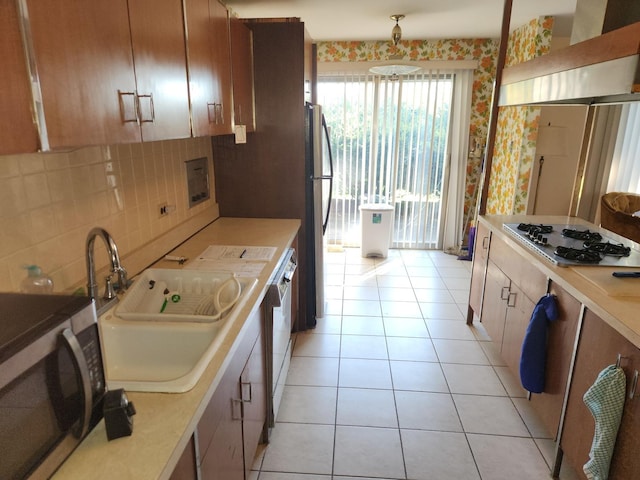 kitchen with a sink, range hood, stainless steel appliances, light tile patterned floors, and decorative backsplash