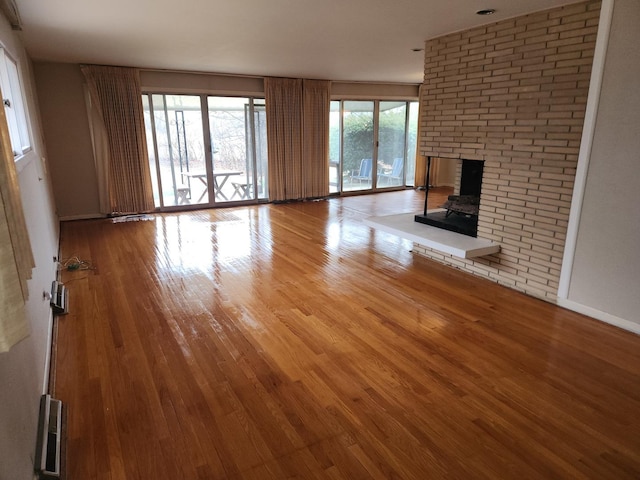 unfurnished living room with a brick fireplace, baseboards, and hardwood / wood-style floors